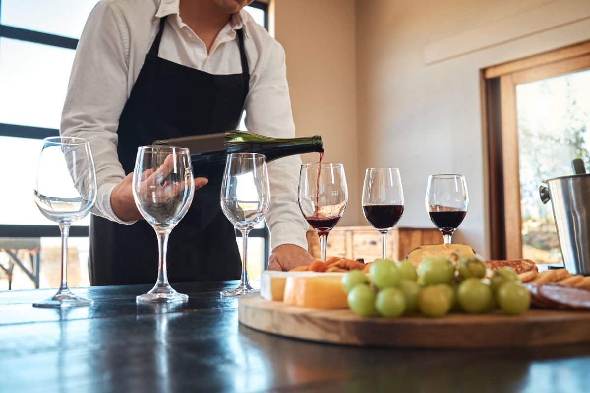 Sommelier schenkt rode wijn in elegante glazen naast een plank met kaas en druiven